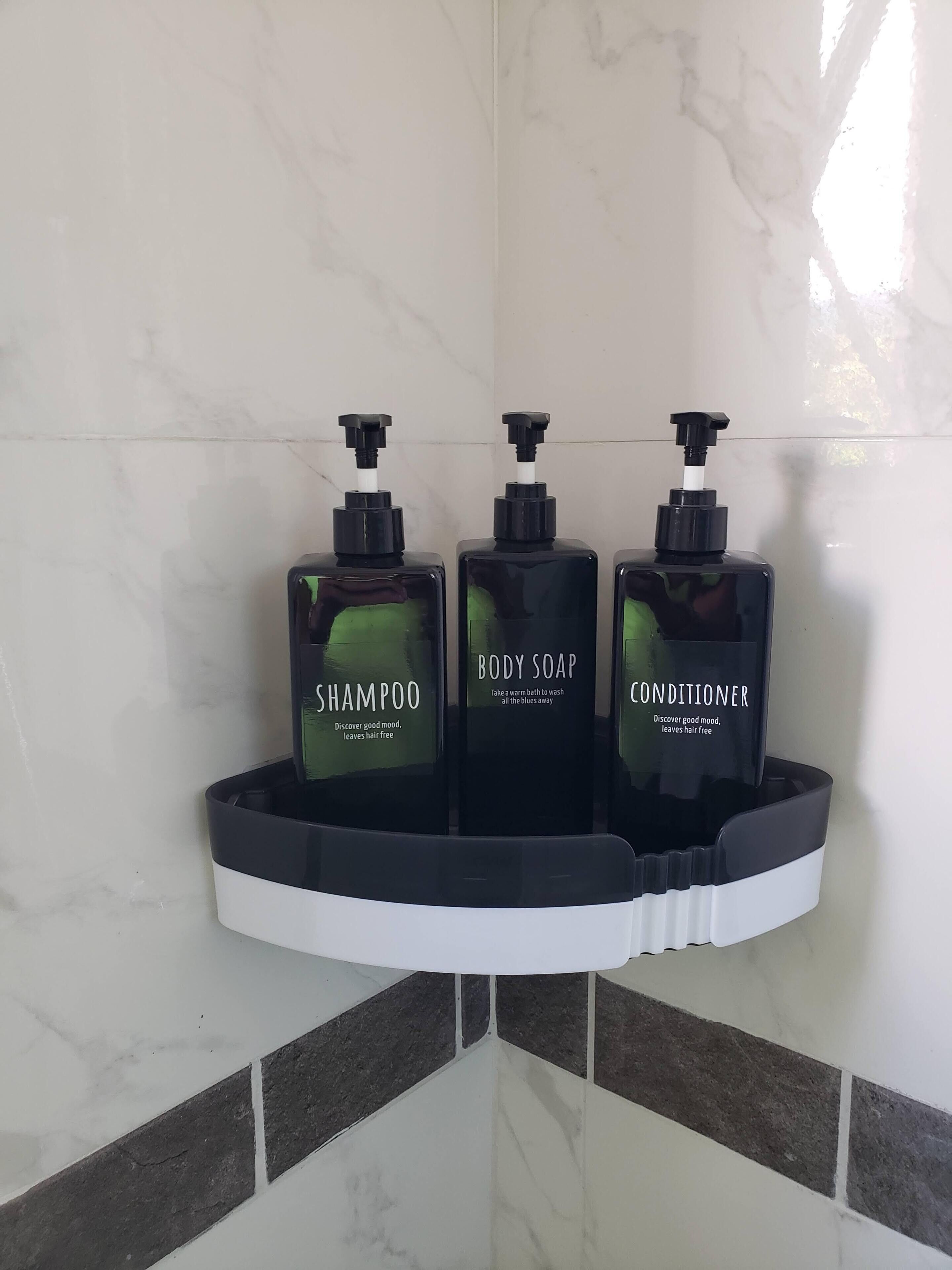 Dans un coin de la salle de bain, on trouve une étagère noire qui sert de présentoir pour trois flacons de savon : un shampoing, un savon pour le corps et un après-shampoing.