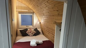 Un dormitorio con techo inclinado, paredes de madera, una ventana, una cama con almohadas y una toalla enrollada.
