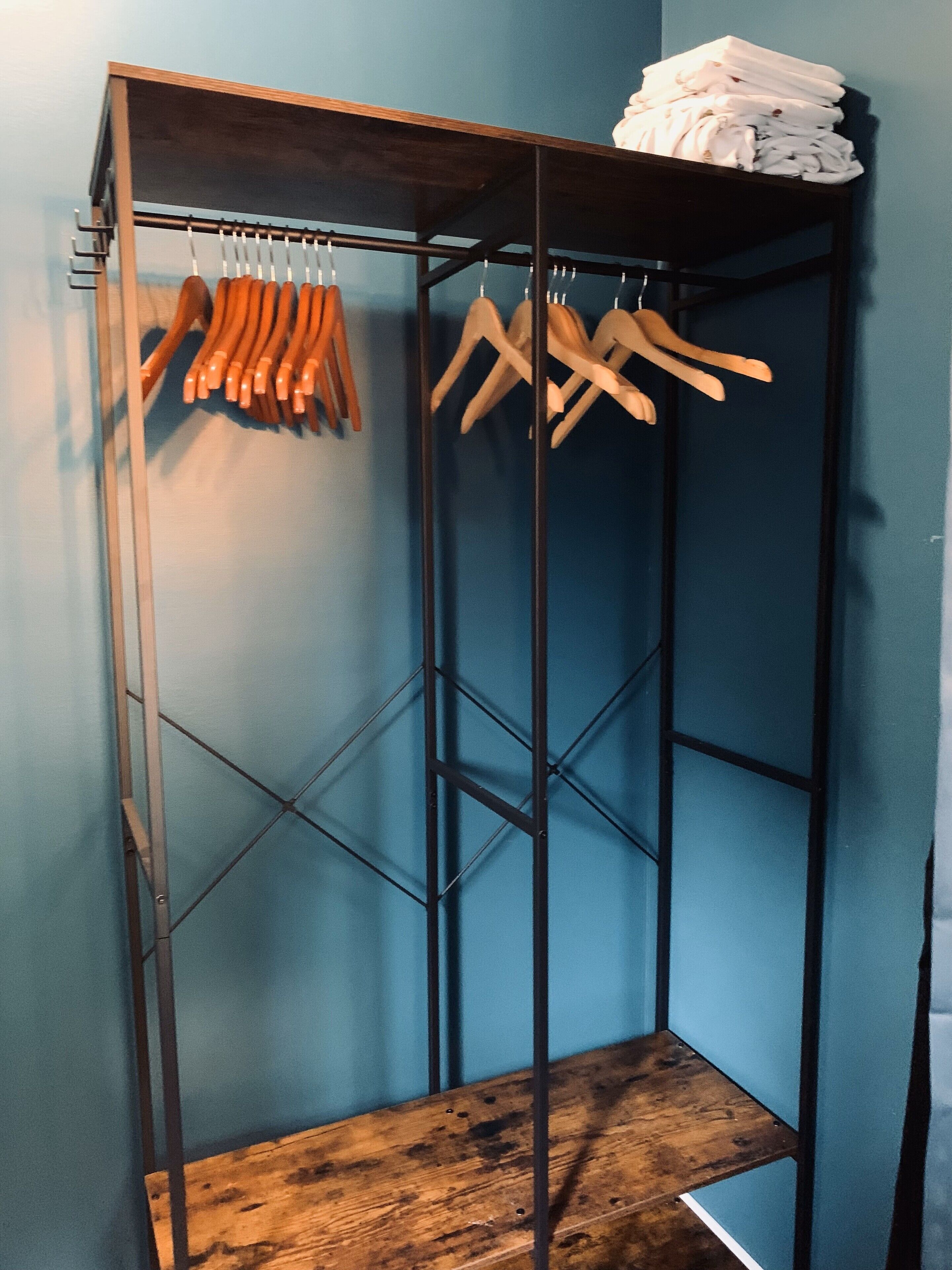 Un'unità di scaffalature metalliche con grucce in legno e una pila di asciugamani bianchi sopra.