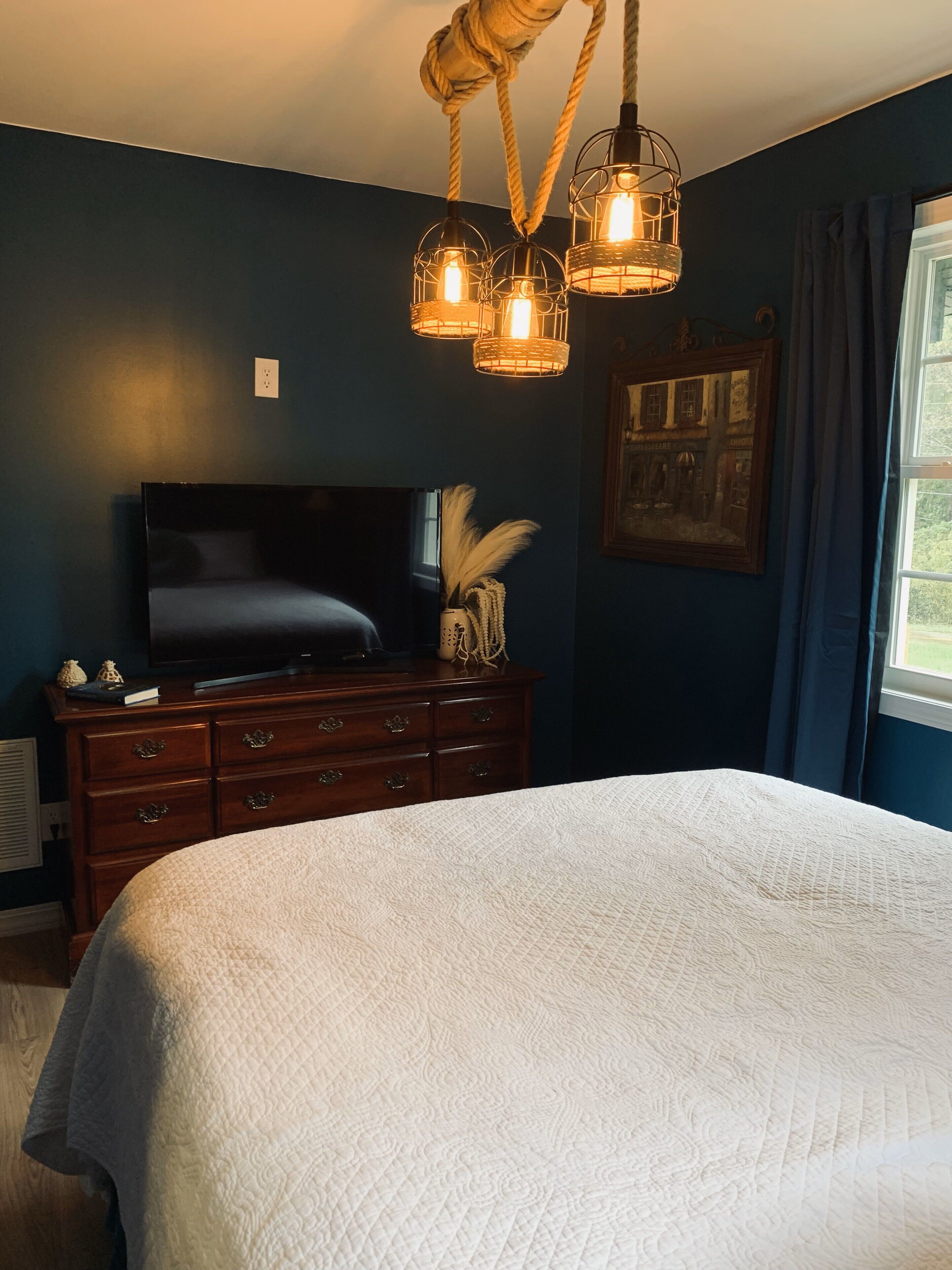 A bedroom with a large bed, a dresser, a television, and a painting on the wall.