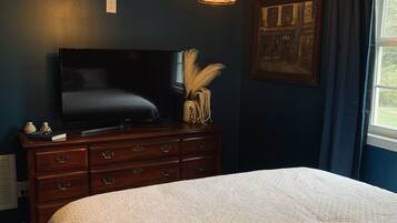 A bedroom with a large bed, a dresser, a television, and a painting on the wall.