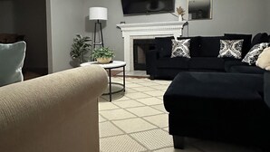 Un salon doté d’un ventilateur de plafond, d’une cheminée, d’un téléviseur fixé au mur et d’un canapé agrémenté de coussins à motifs.