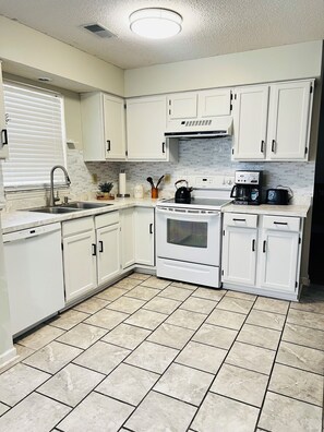 A kitchen with white cabinets, a stove, a coffee maker, and a kettle. - Modern house in North Charleston (Charleston)