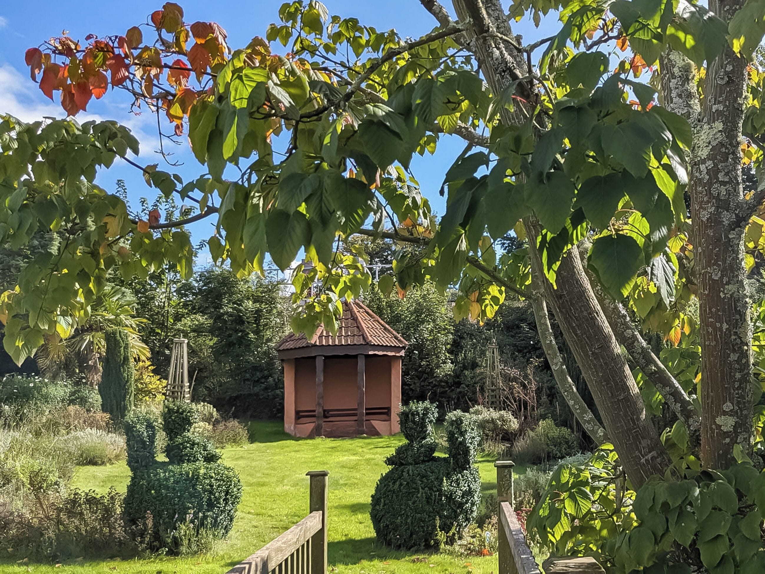 A garden with a gazebo, neatly trimmed hedges, and a variety of trees.