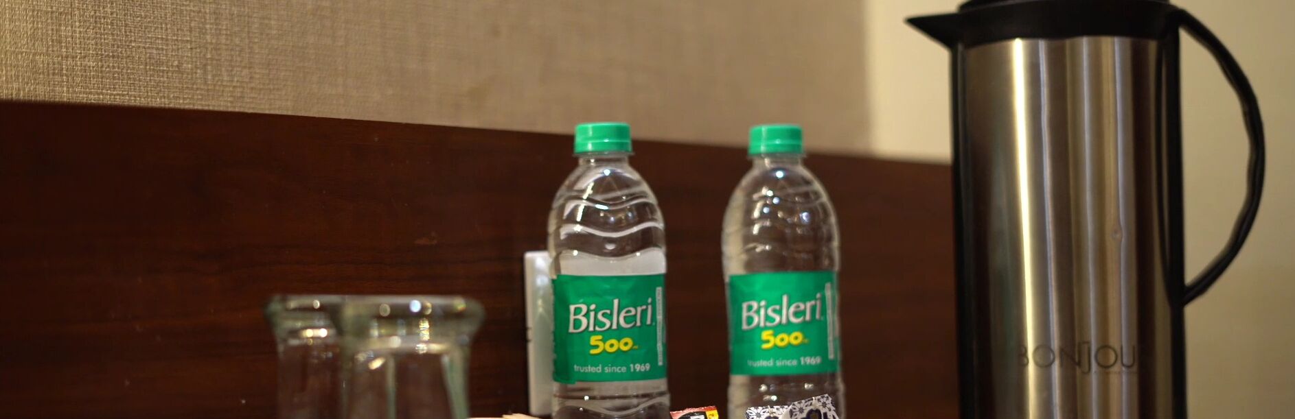 Duas garrafas de água Bisleri de 500ml e uma chaleira elétrica de aço inoxidável sobre uma superfície de madeira.