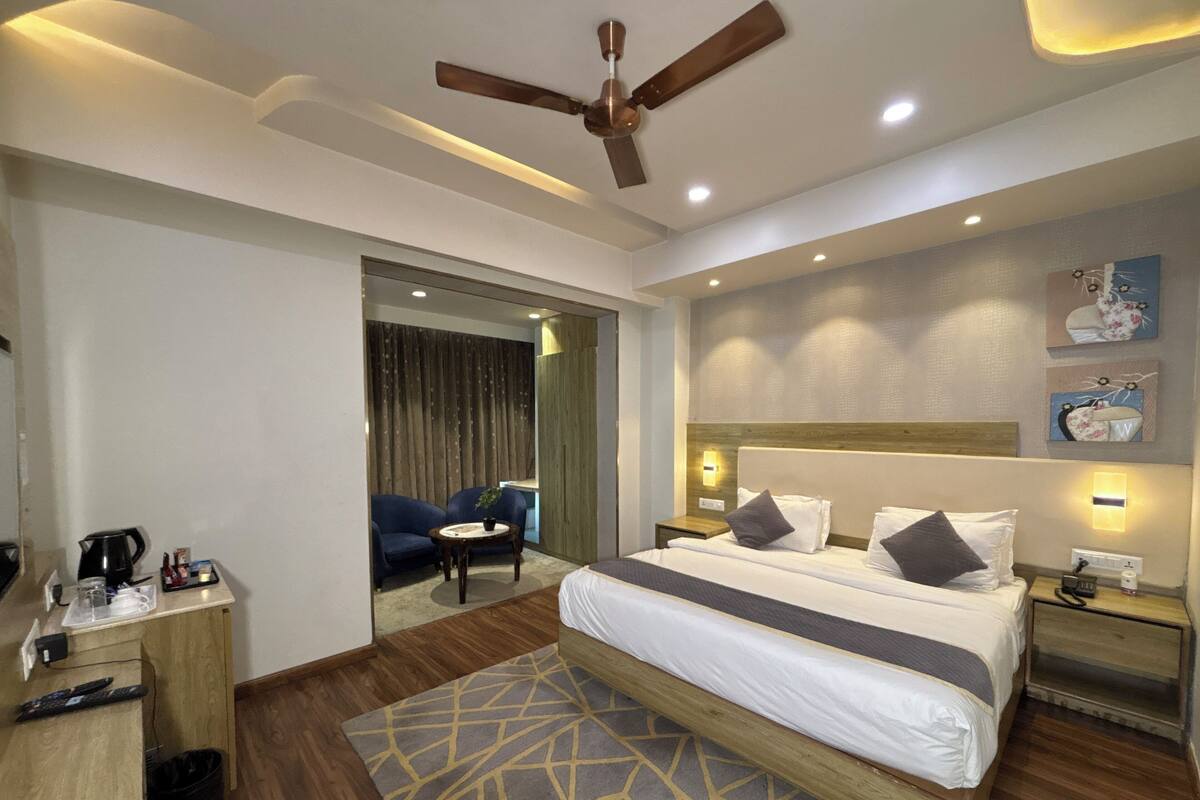 A modern hotel room with a bed, bedside tables, a desk, a ceiling fan, and a view of the hallway.