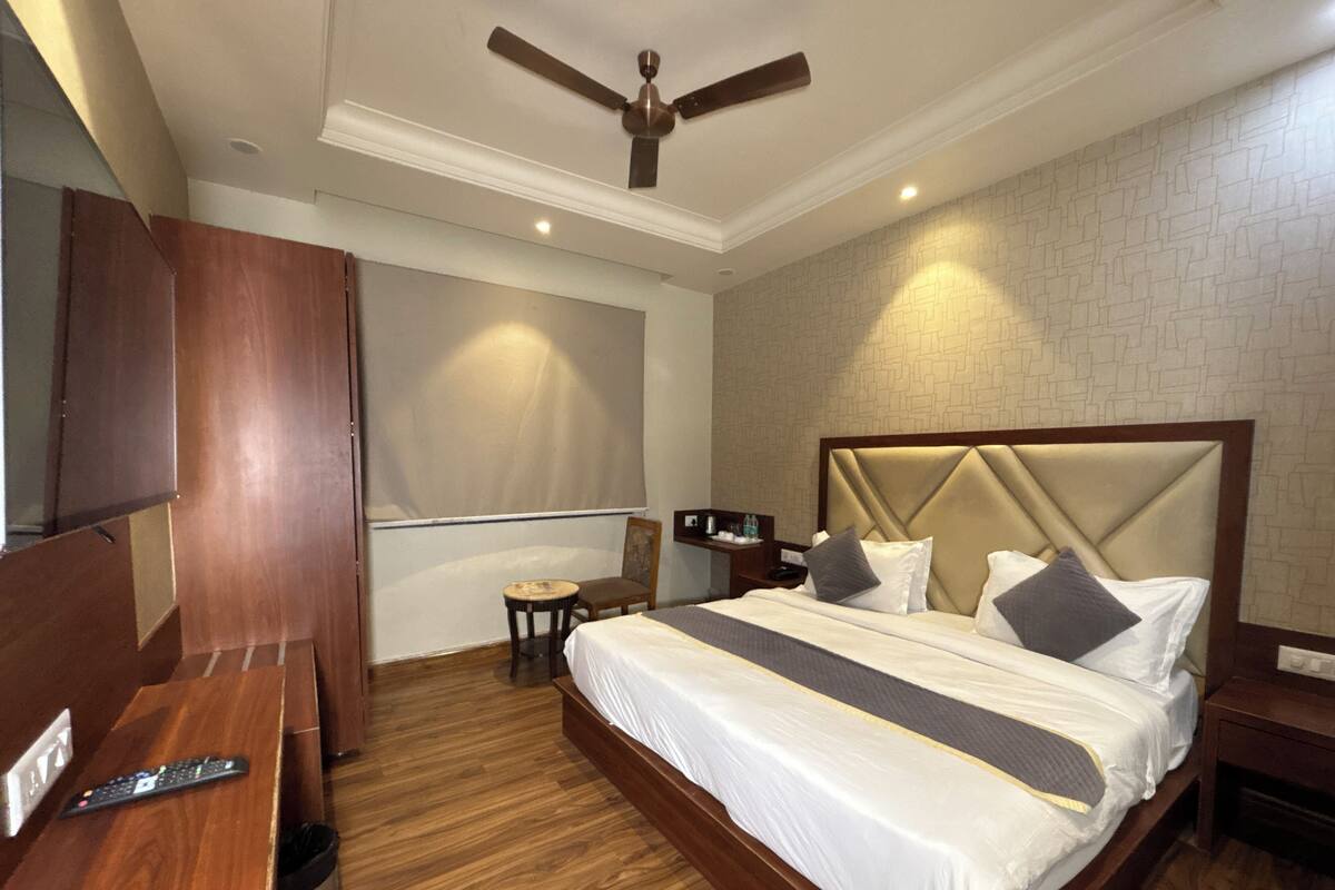 A hotel room with a large bed, wooden floor, a ceiling fan, a TV, and a small table with a chair.