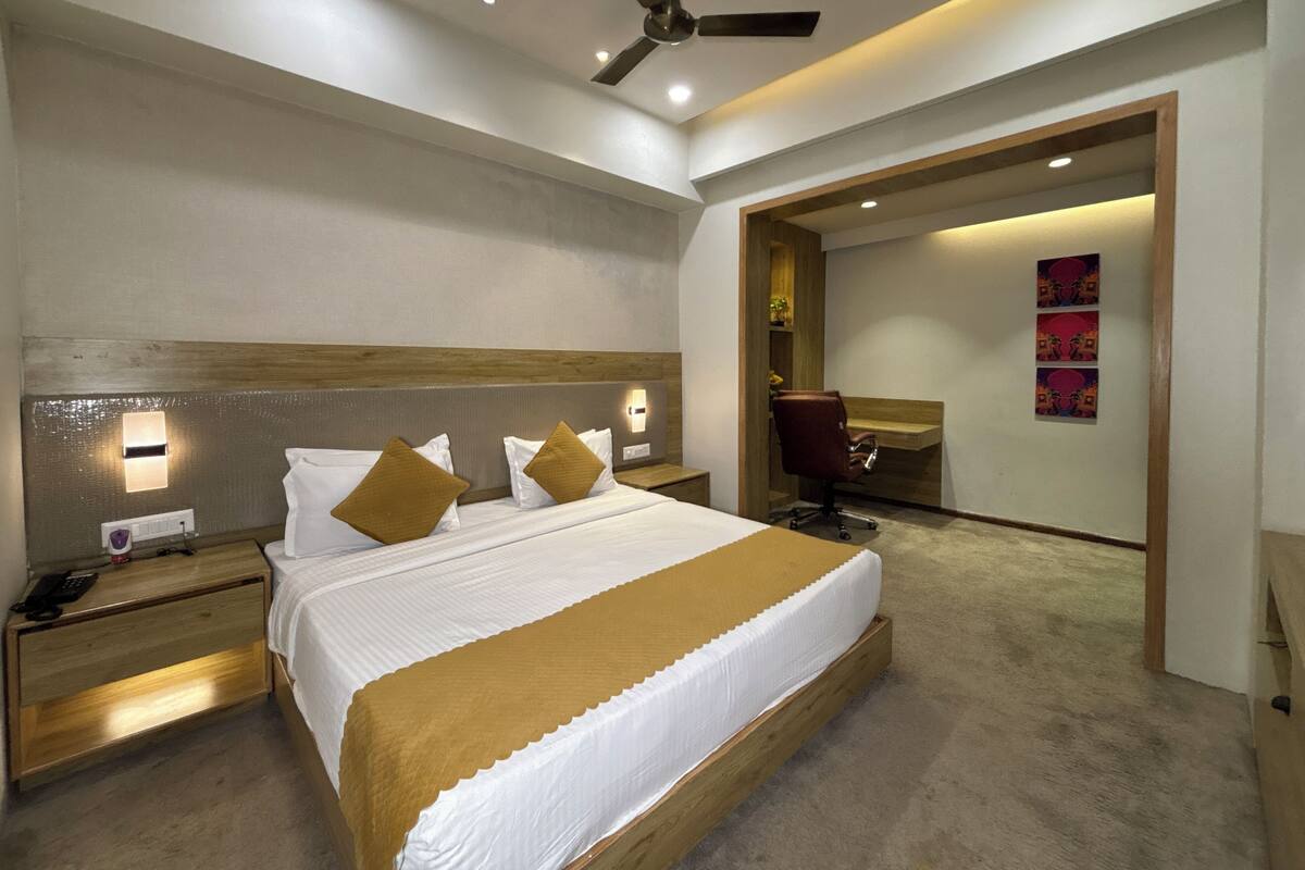 A modern hotel room with a large bed, a desk, a chair, and a ceiling fan.