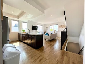 A modern kitchen with a central island, a dining area with a sofa, and a staircase leading to an upper level. - Sainted Ktown Abode + Private Rooftop Deck (Los Angeles)