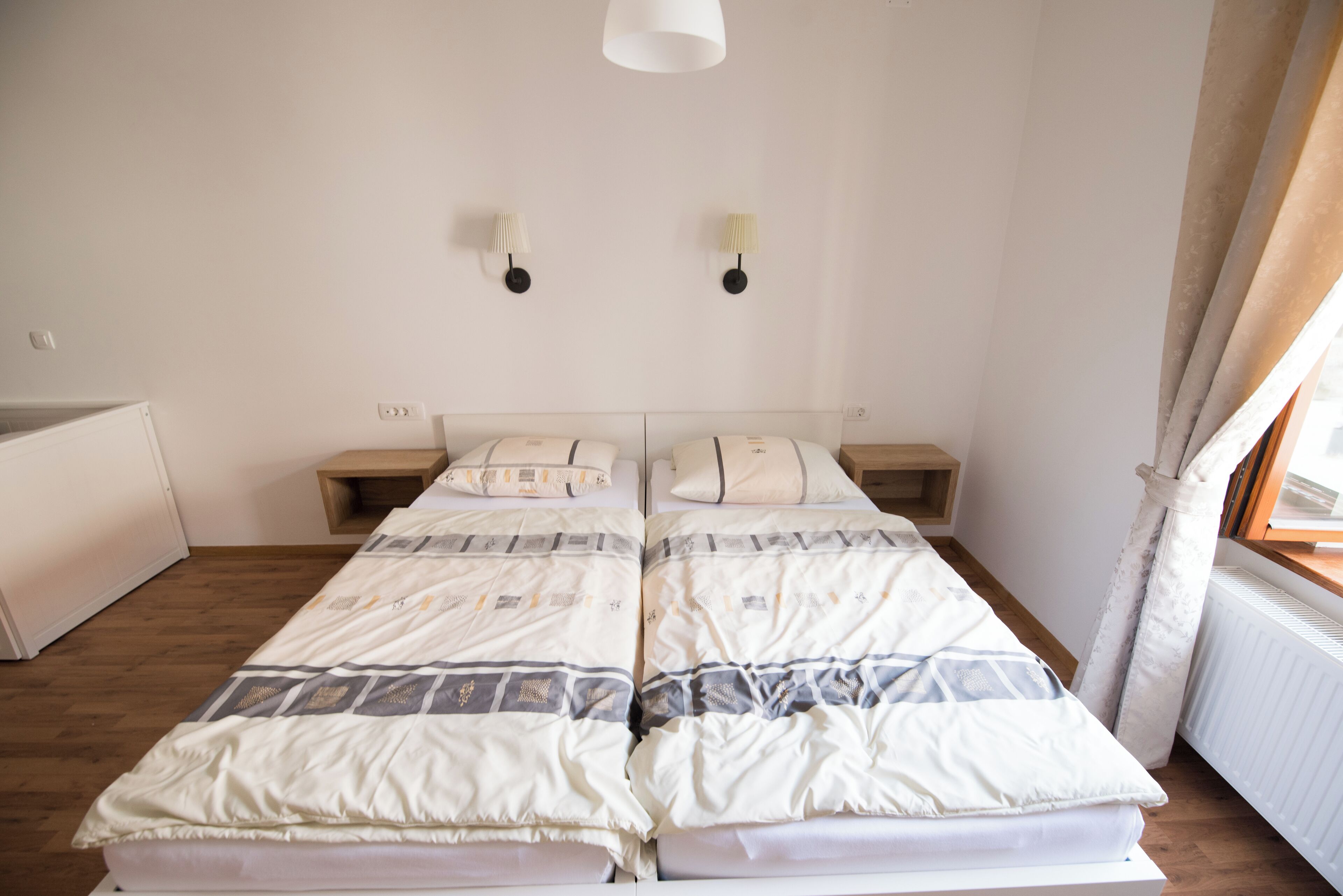 Un letto matrimoniale con copripiumino decorato, comodini, lampade a parete e una finestra con tende.