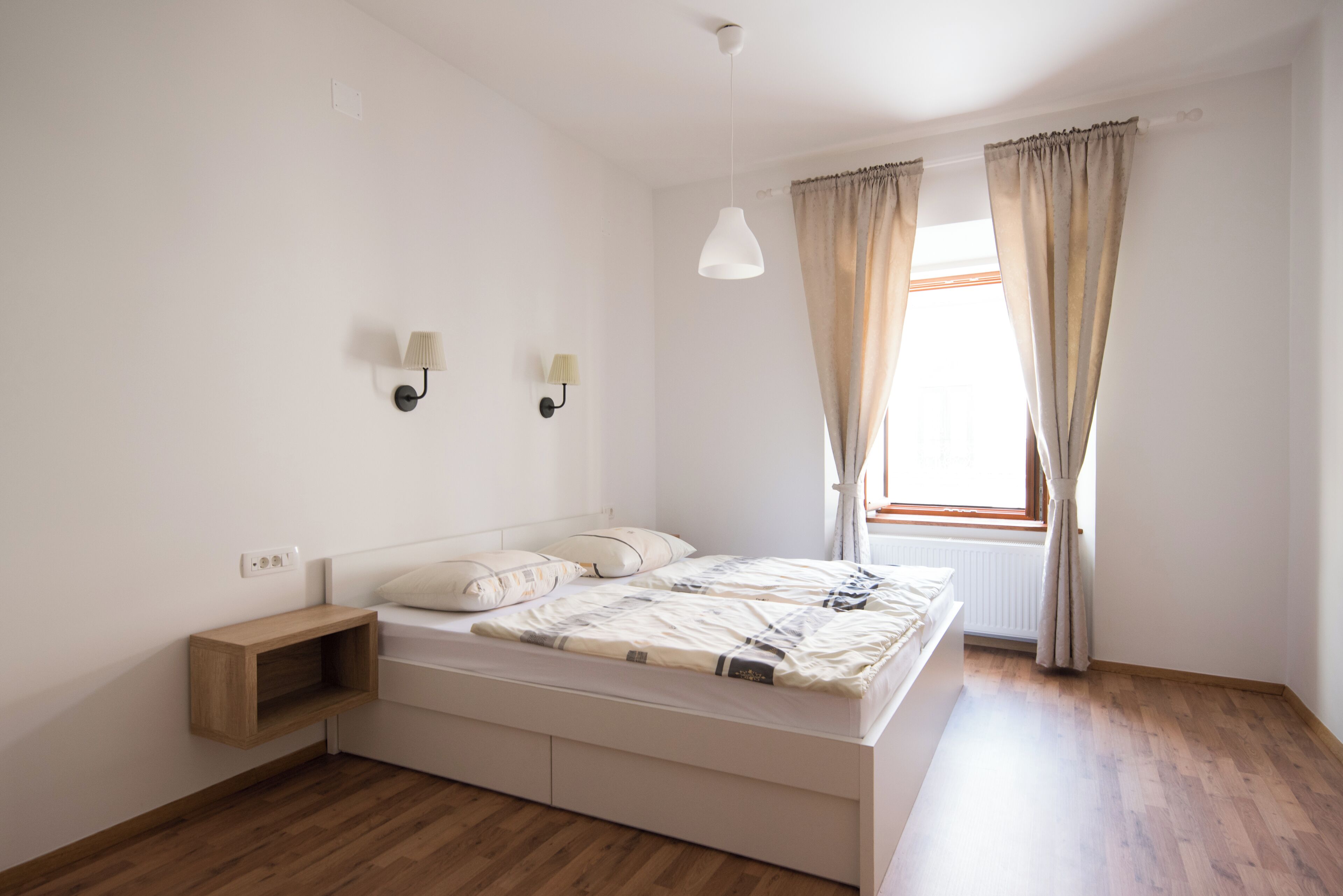 A bedroom with a bed, bedside lamps, a nightstand, and a window with curtains.