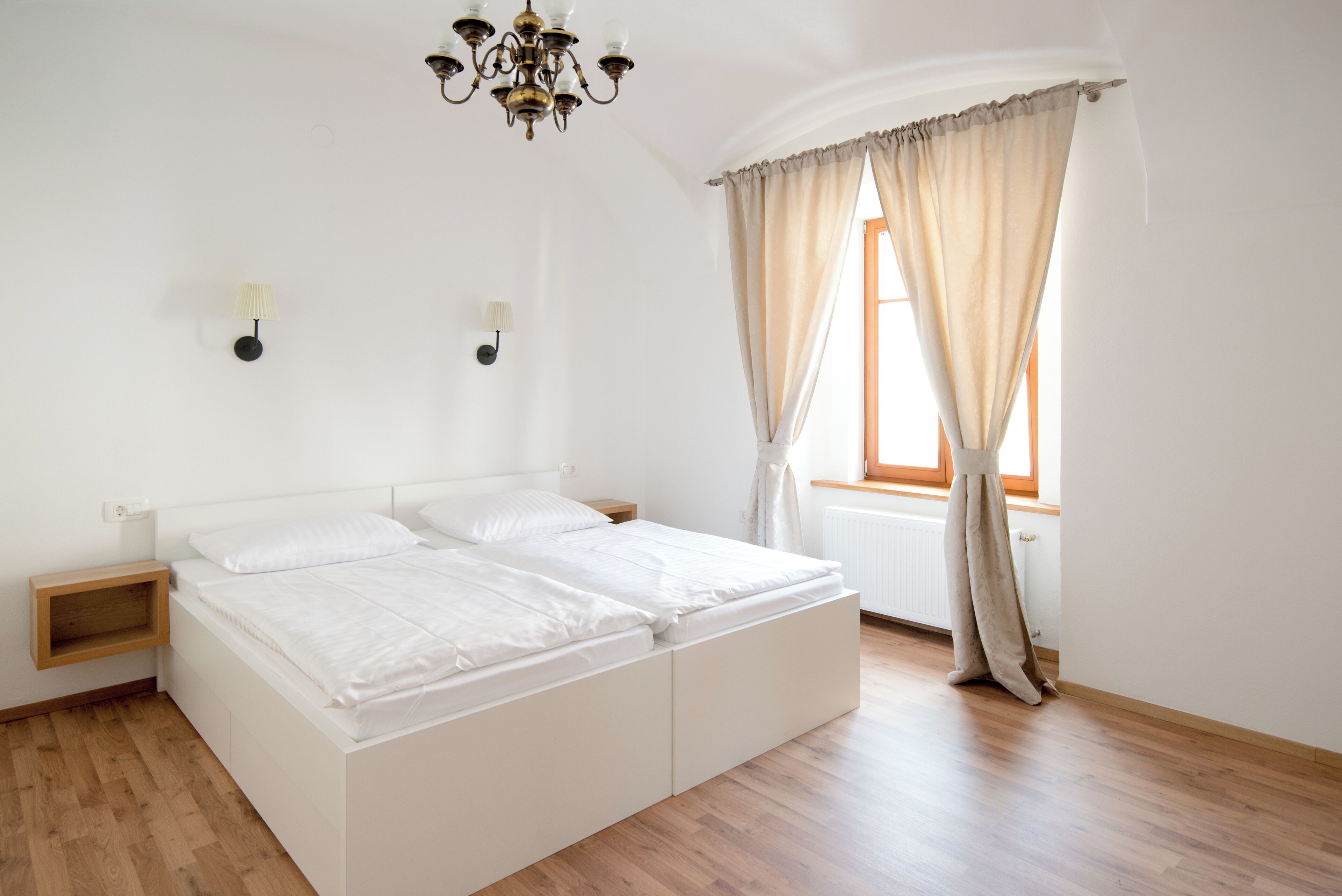 Une chambre à coucher avec un lit double, une table de chevet, une lampe fixée au mur et une fenêtre avec des rideaux.