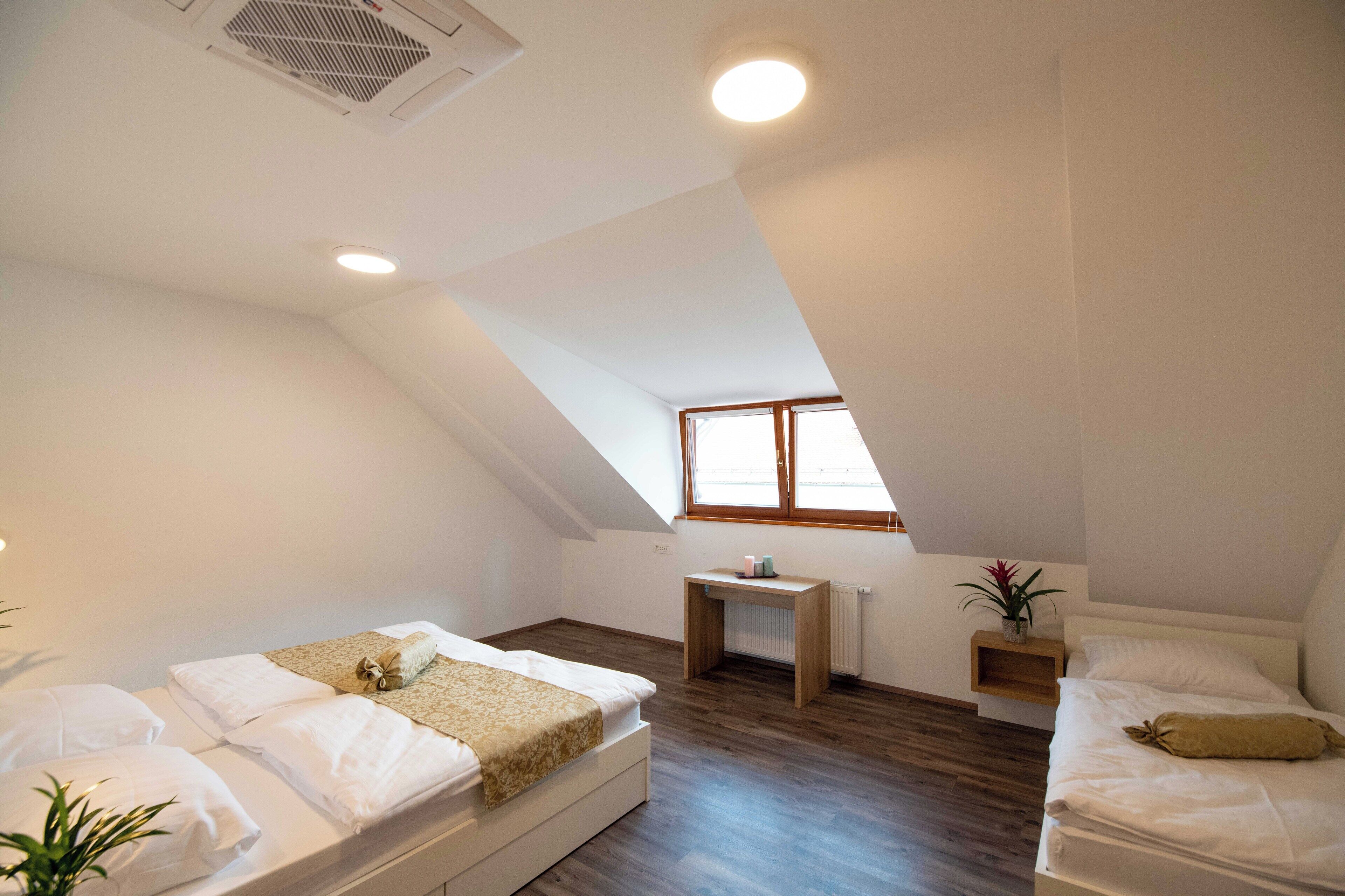 A modern, well-lit bedroom with two beds, a small desk, and a radiator.