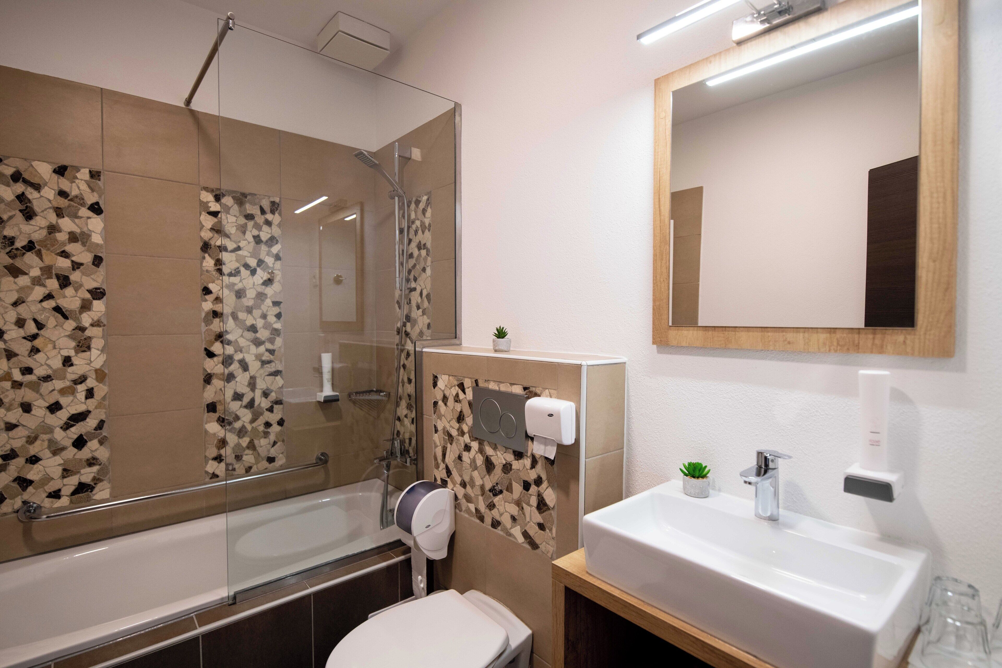 Un baño moderno con cabina de ducha de vidrio, inodoro, lavamanos con espejo y una planta pequeña en la encimera.