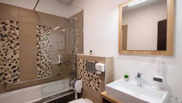 Un baño moderno con cabina de ducha de vidrio, inodoro, lavamanos con espejo y una planta pequeña en la encimera.