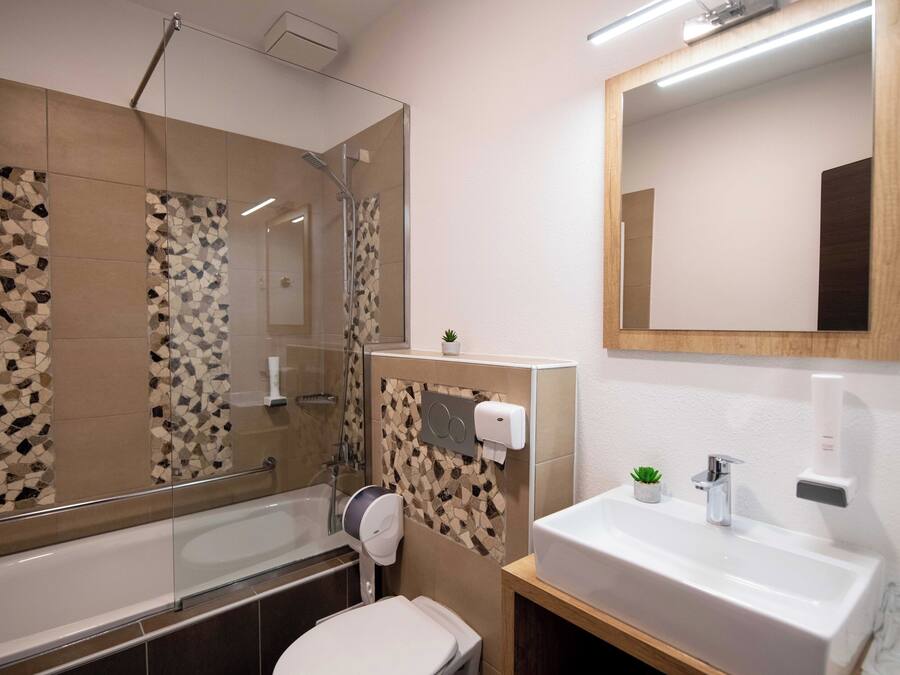 Un baño moderno con cabina de ducha de vidrio, inodoro, lavamanos con espejo y una planta pequeña en la encimera.