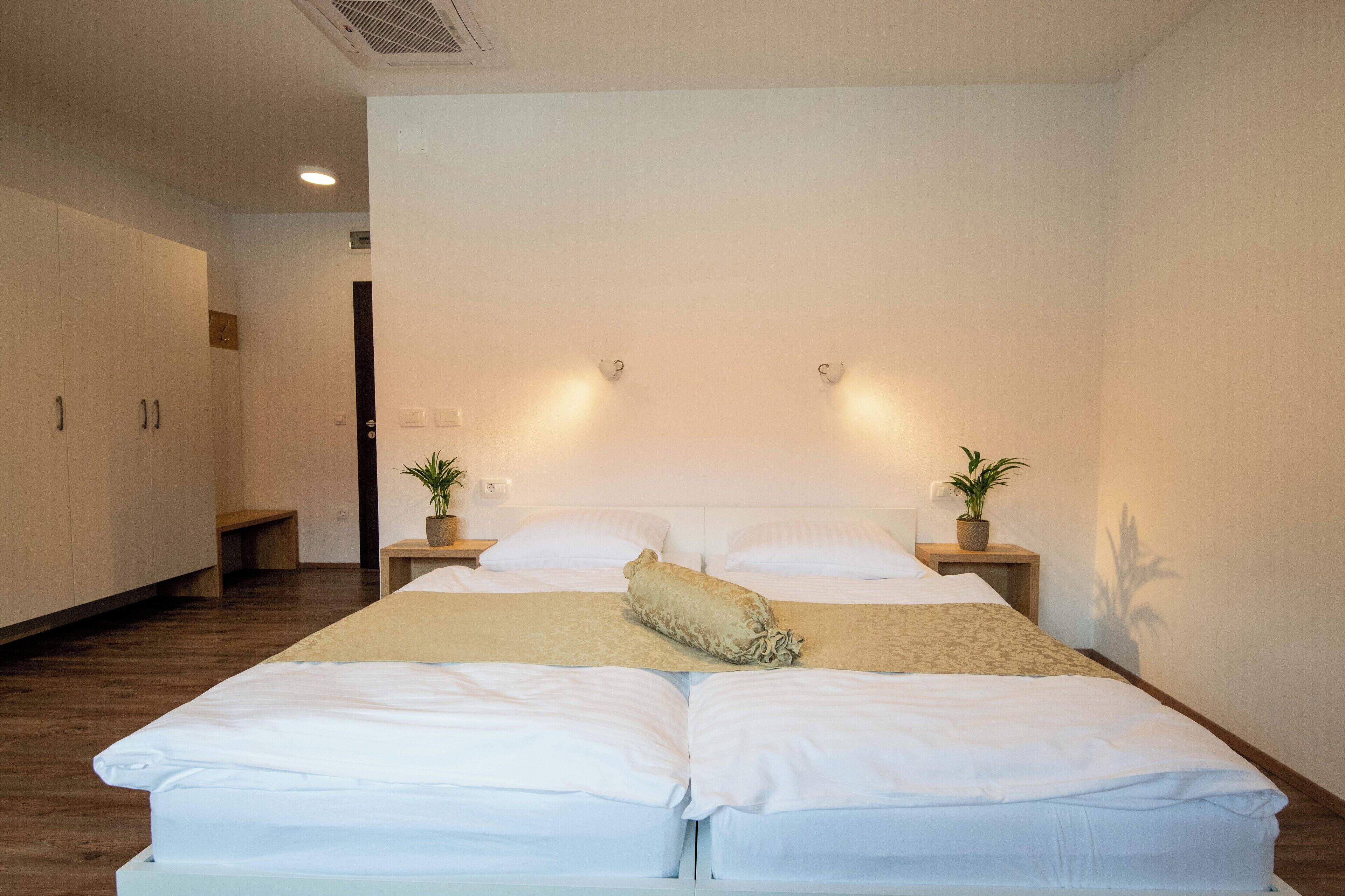 Une chambre à coucher bien aménagée, avec un grand lit, des tables de chevet ornées de plantes en pot et un banc placé dans un coin.
