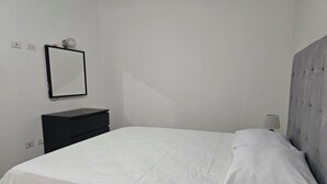 Un dormitorio con cama, mesita de noche, lámpara y espejo adosado a la pared.