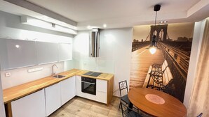Una cocina moderna con armarios blancos, encimera de madera y horno empotrado. Hay una zona de comedor con una mesa redonda y sillas, y un ventanal con vistas a la ciudad.
