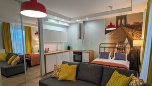 Habitación de hotel compacta con sofá, cama, kitchenette y un espejo grande que refleja el cuarto.