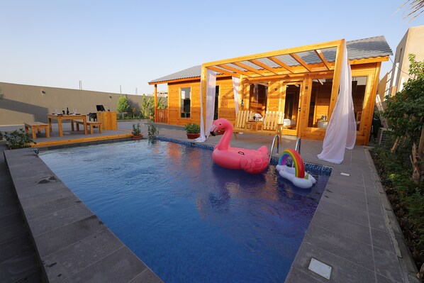 Eine Holzhütte mit Pool, einem Flamingo-Schwimmpflege und einem Regenbogen-Schwimmpflege.