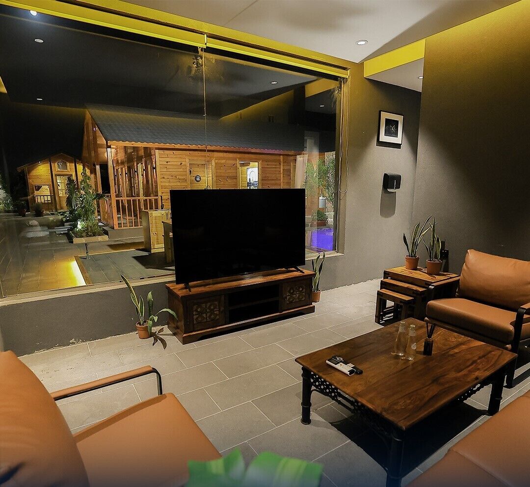 Un salon moderne doté d’un grand téléviseur à écran plat, de meubles en bois et offrant une vue sur un chalet en bois.