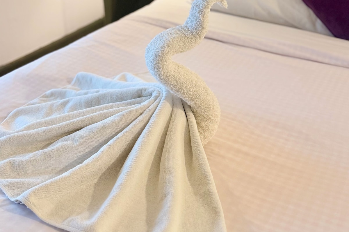 A bed with a towel arranged in a swan shape.