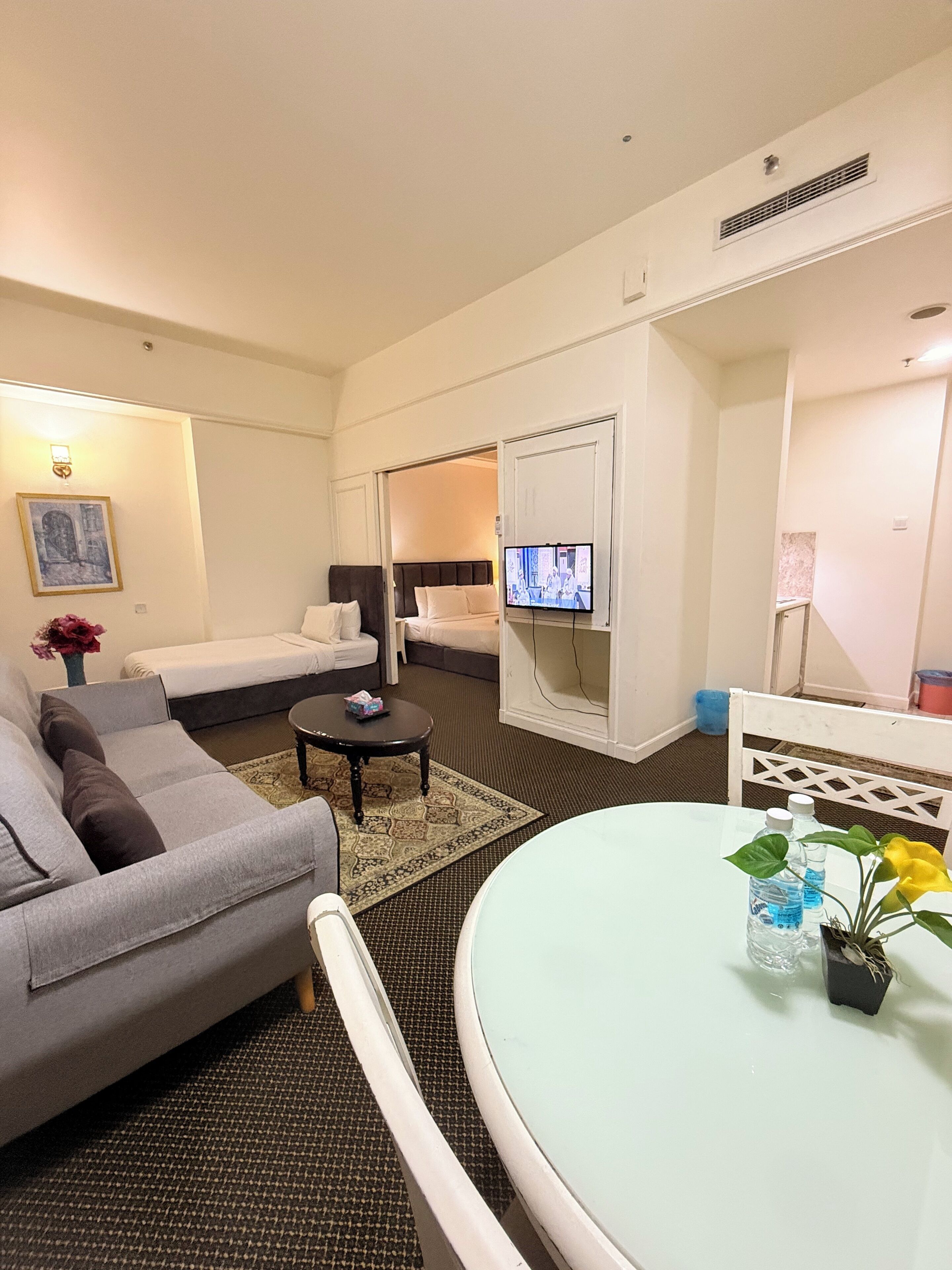 A hotel room with a sofa, a round table, a TV, and a bed with a headboard.