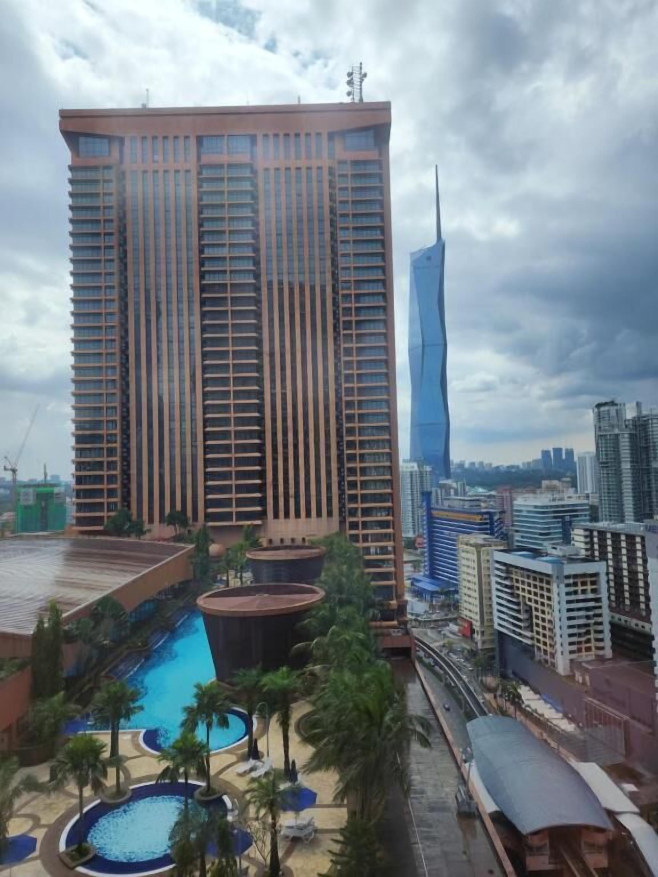 A high-rise hotel with a swimming pool, palm trees, and a view of the city skyline.