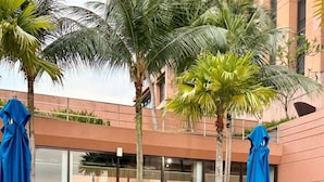 An outdoor patio with tables and chairs, covered by blue umbrellas, and surrounded by palm trees. - KL Grand Service Suite at Times Square (Kuala Lumpur)