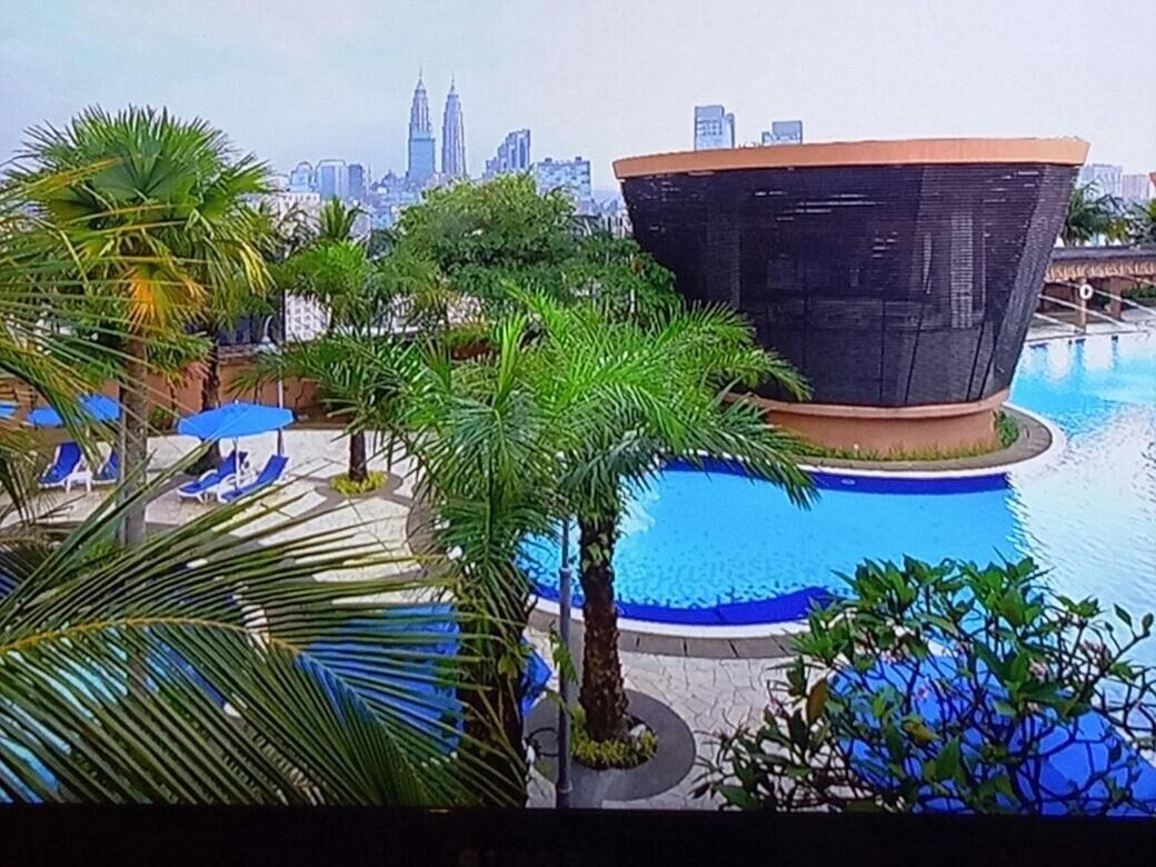 Un área de piscina con sillones de descanso y palmeras, rodeada por un edificio moderno con techo curvo.