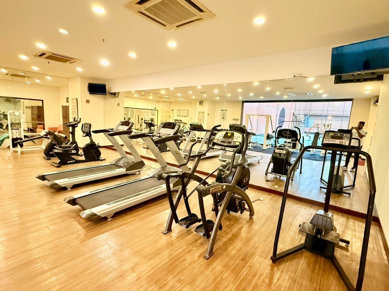 A gym with treadmills, elliptical machines, and a mirrored wall.