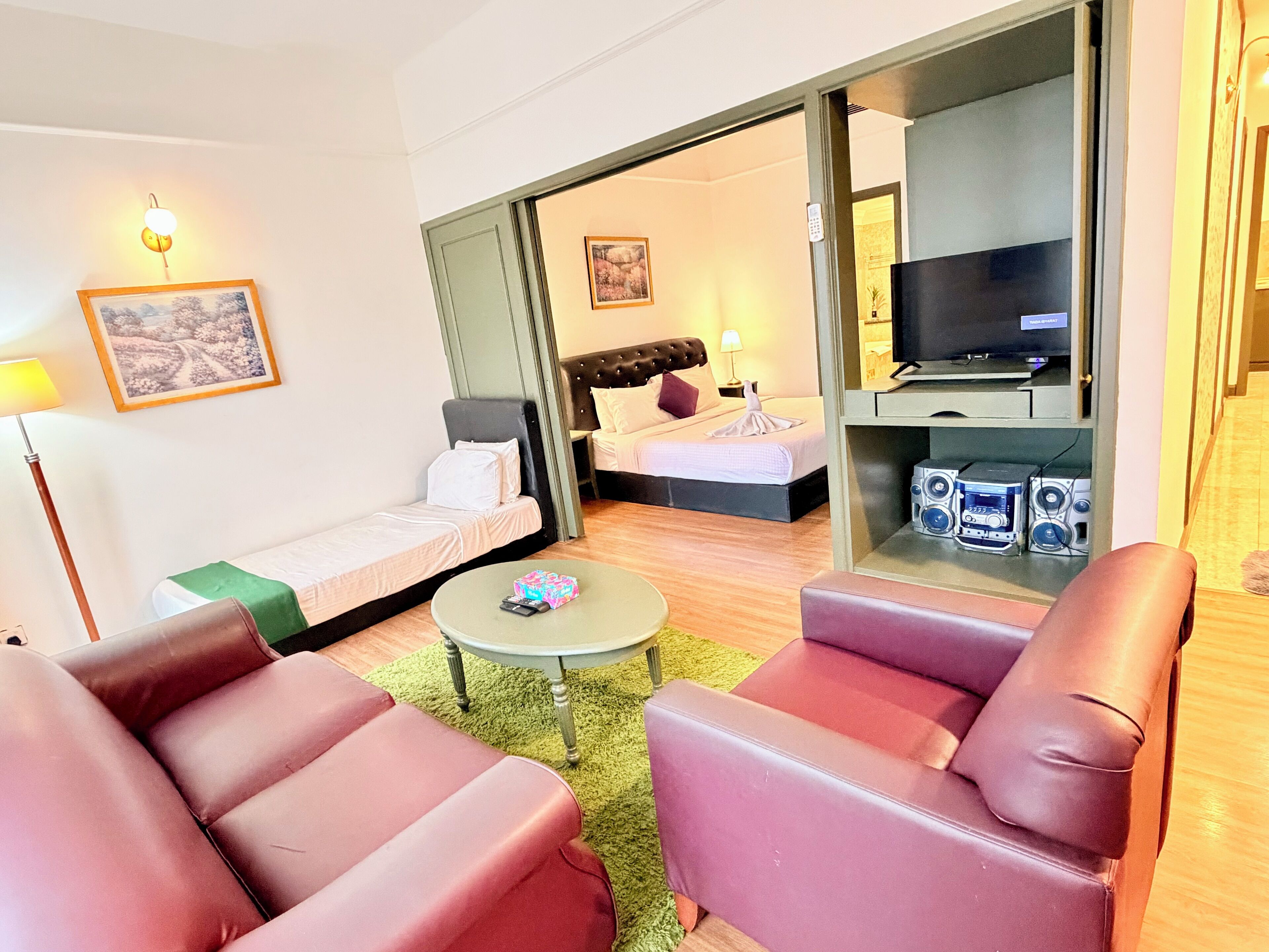 A hotel room with a bed, a sofa, a coffee table, a TV, and a small table with speakers.