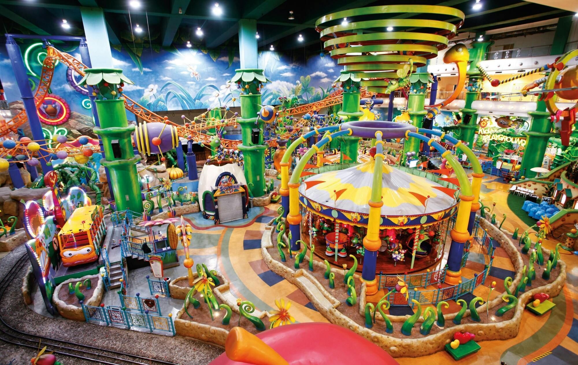 A vibrant indoor play area with various colorful play structures, a carousel, and a themed mural on the walls.