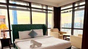 A hotel room with a large bed, a green upholstered headboard, a white bedspread, a blue pillow, a small round table, and a chair. - KL Grand Service Suite at Times Square (Kuala Lumpur)