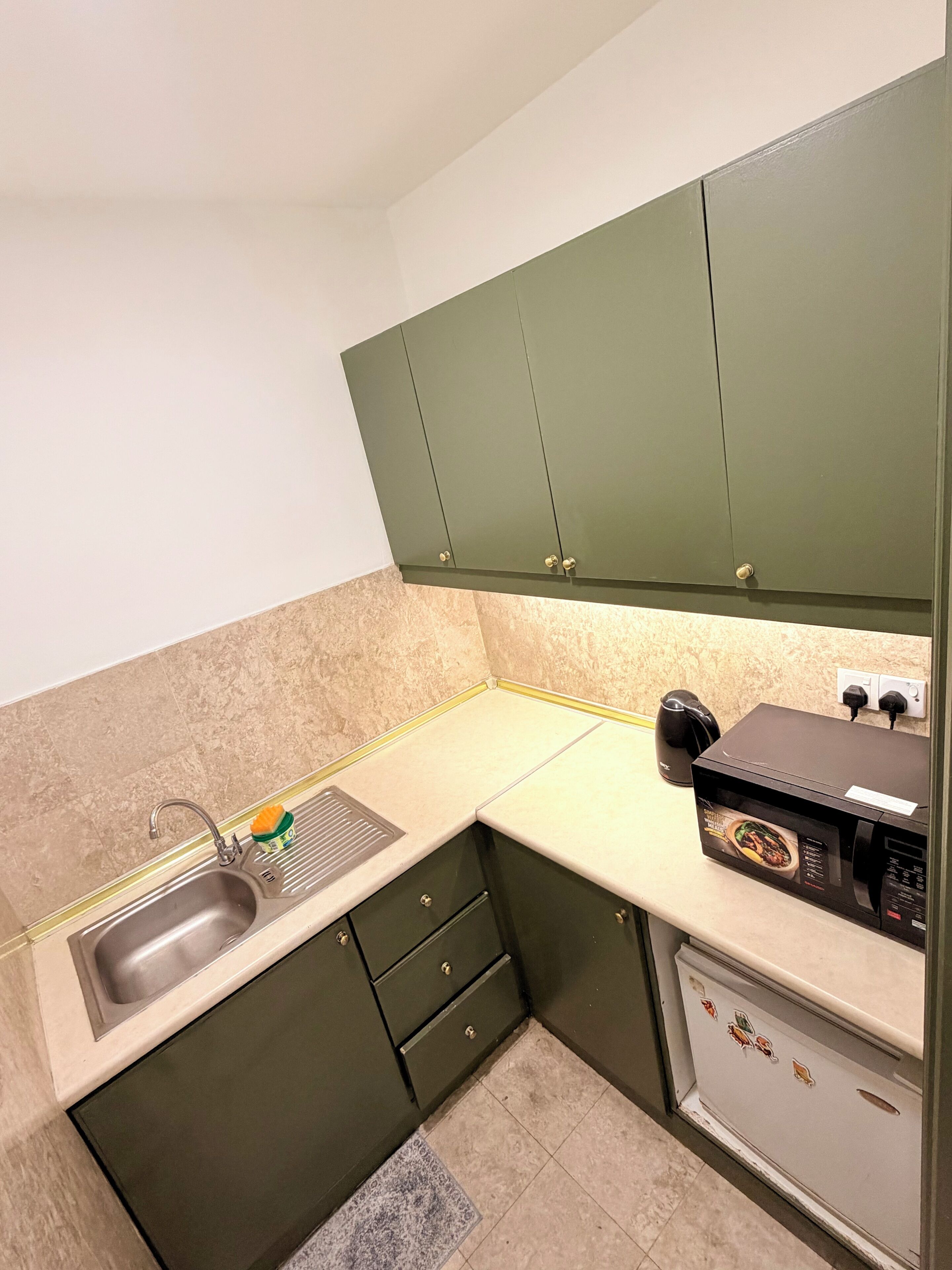 A kitchen with green cabinets, a sink, a microwave, and a kettle.
