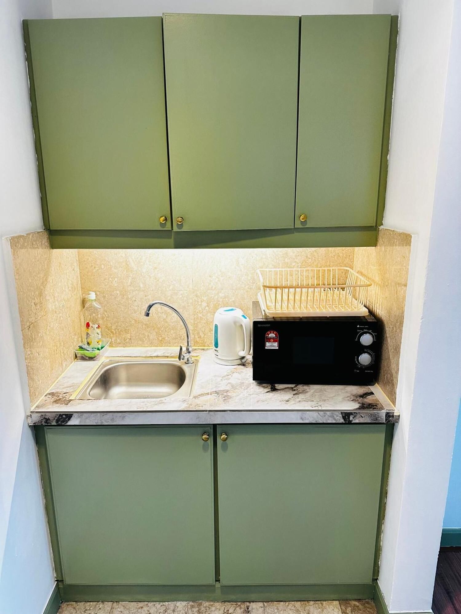 A small kitchen with green cabinets, a sink, a kettle, and a toaster.