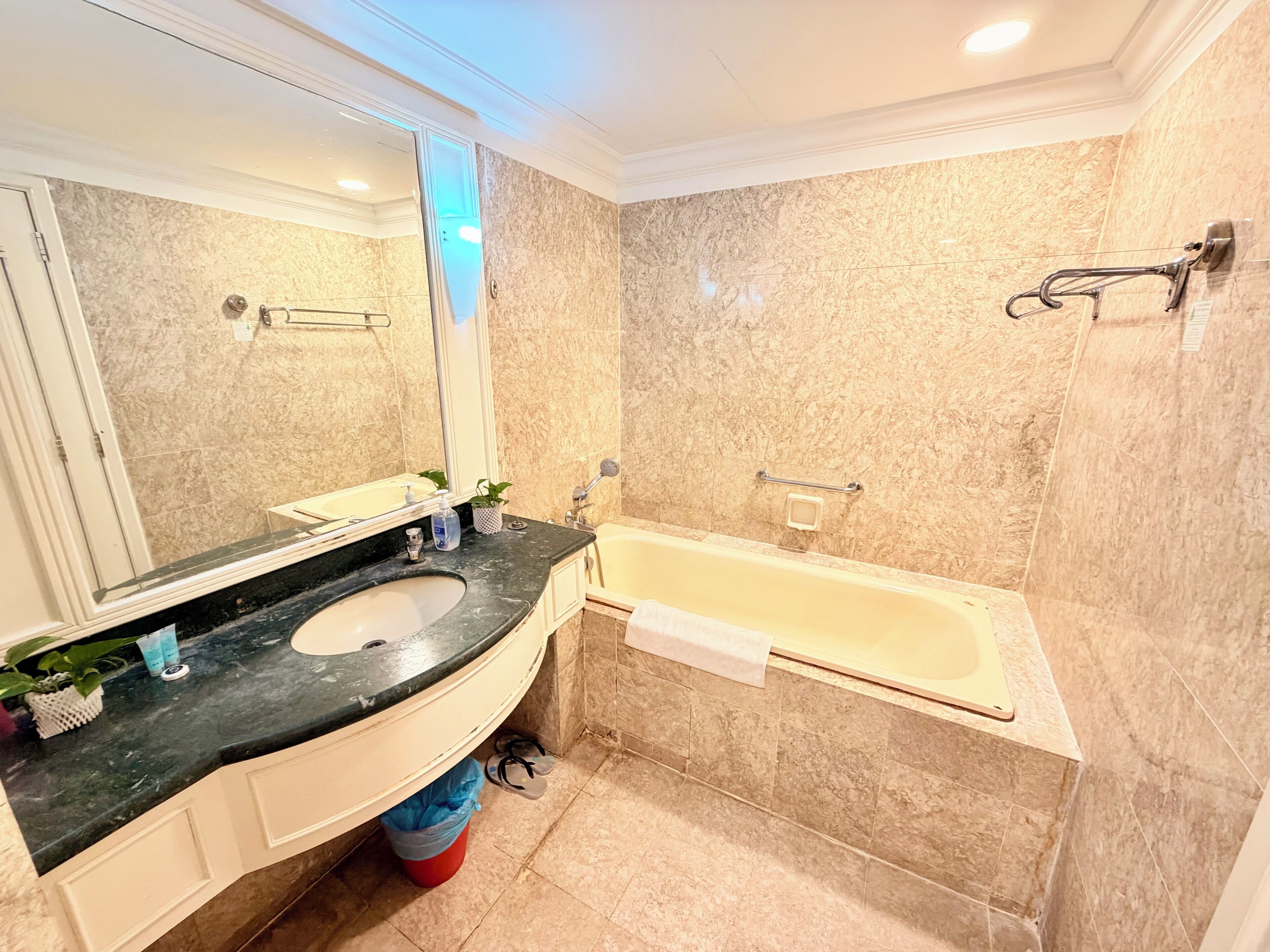 A bathroom with a marble wall, a sink, a mirror, and a bathtub.