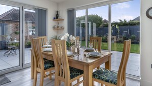 A dining area with a large table, wooden chairs, and a view of the garden through large windows.