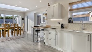 A modern kitchen with white cabinets, a dining area with wooden chairs, and a large window providing natural light.