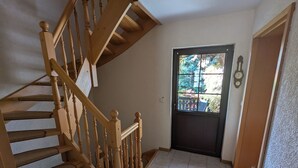 A wooden staircase leading to a dark door with a window, a clock on the wall, and a tiled floor. - Family-friendly vacation home Bornholzweg in Quedlinburg - 157 sqm (Quedlinburg)