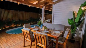 An outdoor dining area with a pool, wooden deck, and a covered section with a white wall. - New Luxury Villa 8 min beach walk Pool+Grill Near West Bay (Roatan)