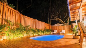 A wooden deck with a swimming pool, surrounded by plants and two lounge chairs. - New Luxury Villa 8 min beach walk Pool+Grill Near West Bay (Roatan)
