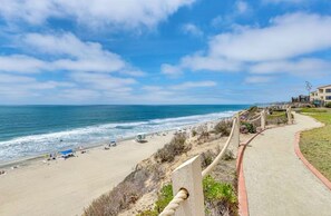 A coastal beach with a paved walkway, beach umbrellas, and a lifeguard tower.