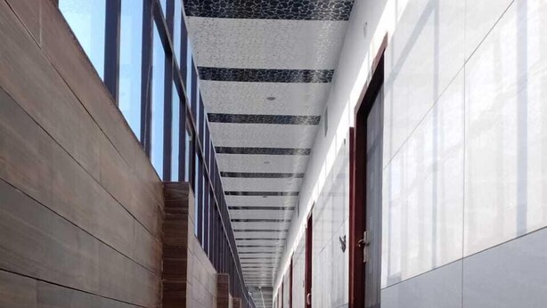 A long, narrow hallway with a polished marble floor, wooden paneling on one side, and a white tiled wall on the other. - Hotel Sunrahi (Nagina)
