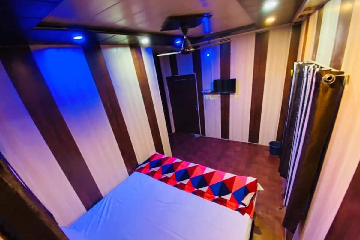 Une pièce avec un lit, un ventilateur de plafond, un téléviseur fixé au mur et une porte.