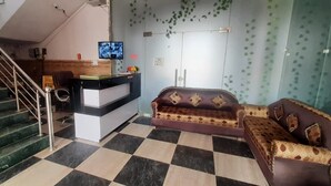 A reception area with a reception desk, a television, a sofa, and a staircase. - Hotel Sunrahi (Nagina)