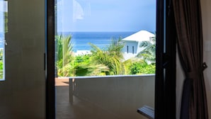 A view from a balcony overlooking a beach with palm trees and a white building in the distance. - One bedroom suite in Punta Sur (Isla Mujeres)