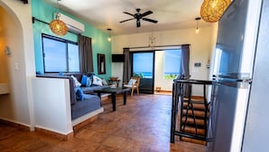 A spacious living area with a sofa, dining table, and a view of the ocean through large windows. - One bedroom suite in Punta Sur (Isla Mujeres)