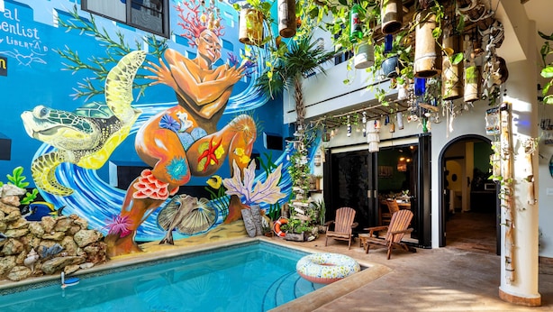 An indoor swimming pool with a mural of sea creatures, surrounded by potted plants and wooden chairs. - One bedroom suite in Punta Sur (Isla Mujeres)